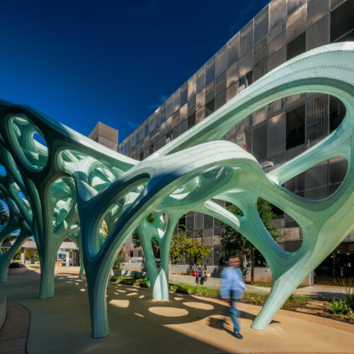 Photograph of large scale light green sculpture with person walking underneath outside the Austin-Bergstrom Airport.