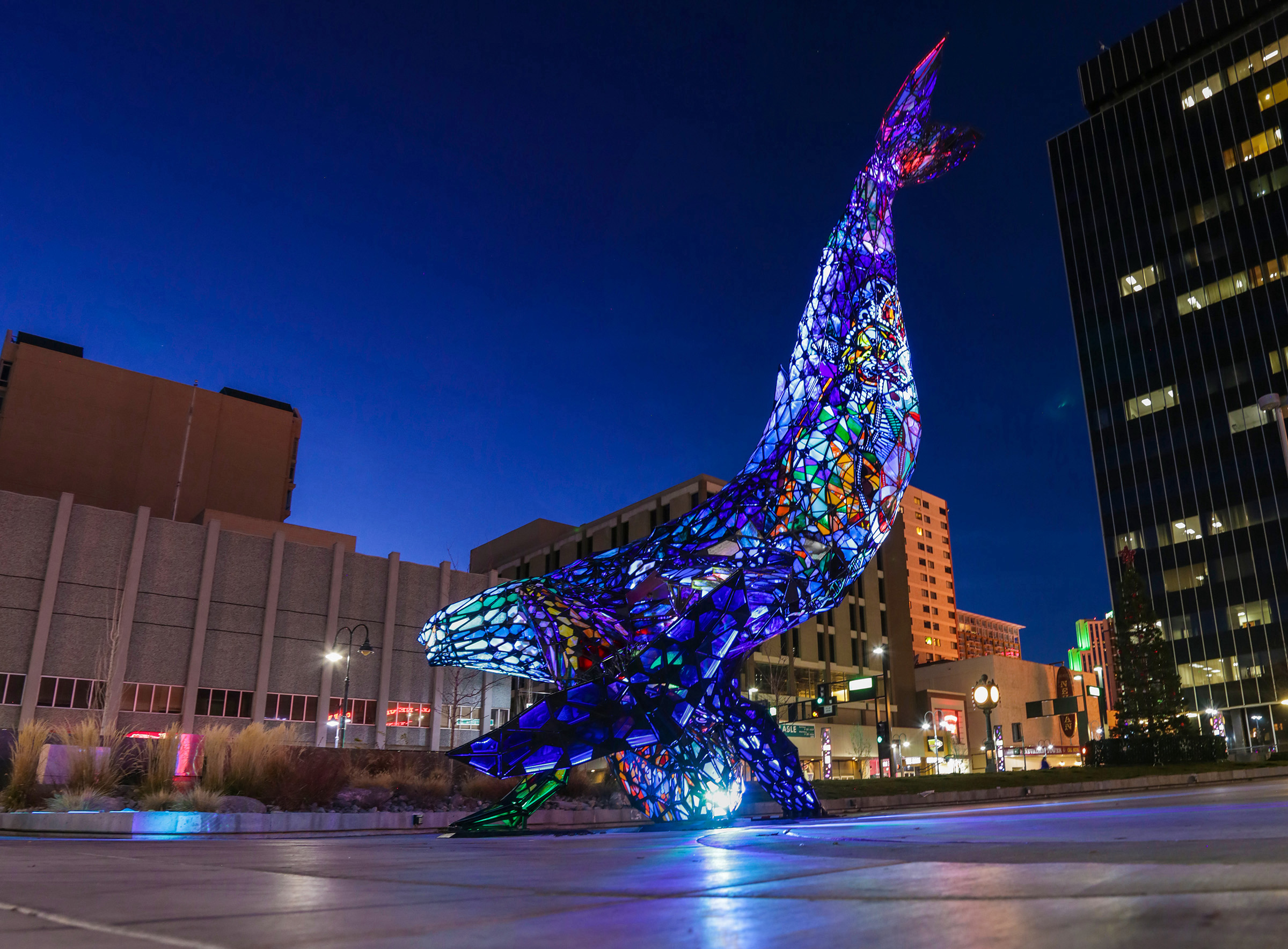 A large colorful blue whale sculpture placed outside in front of a building in the city.