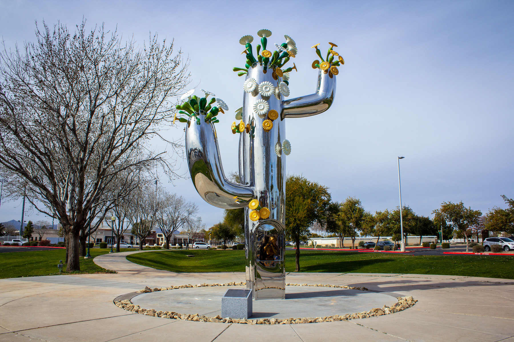 A large metal sculpture of a cactus with flowers growing out of it placed outside a school.