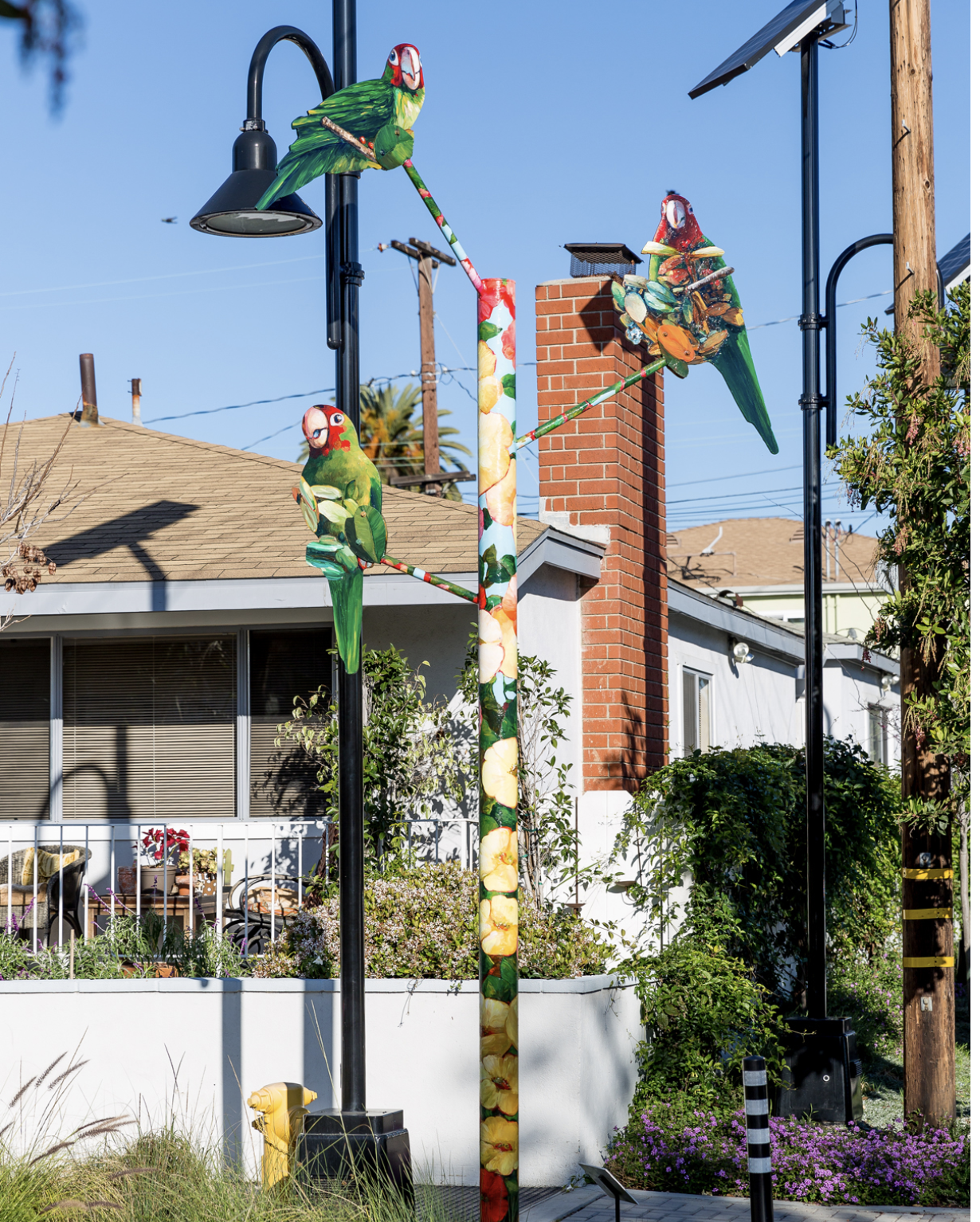 Three colorful parrots sitting on top of a floral post outside in a neighborhood. 