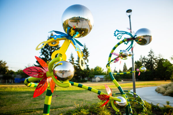 Colorful metal sculptures with reflective silver spheres are displayed in an outdoor setting.