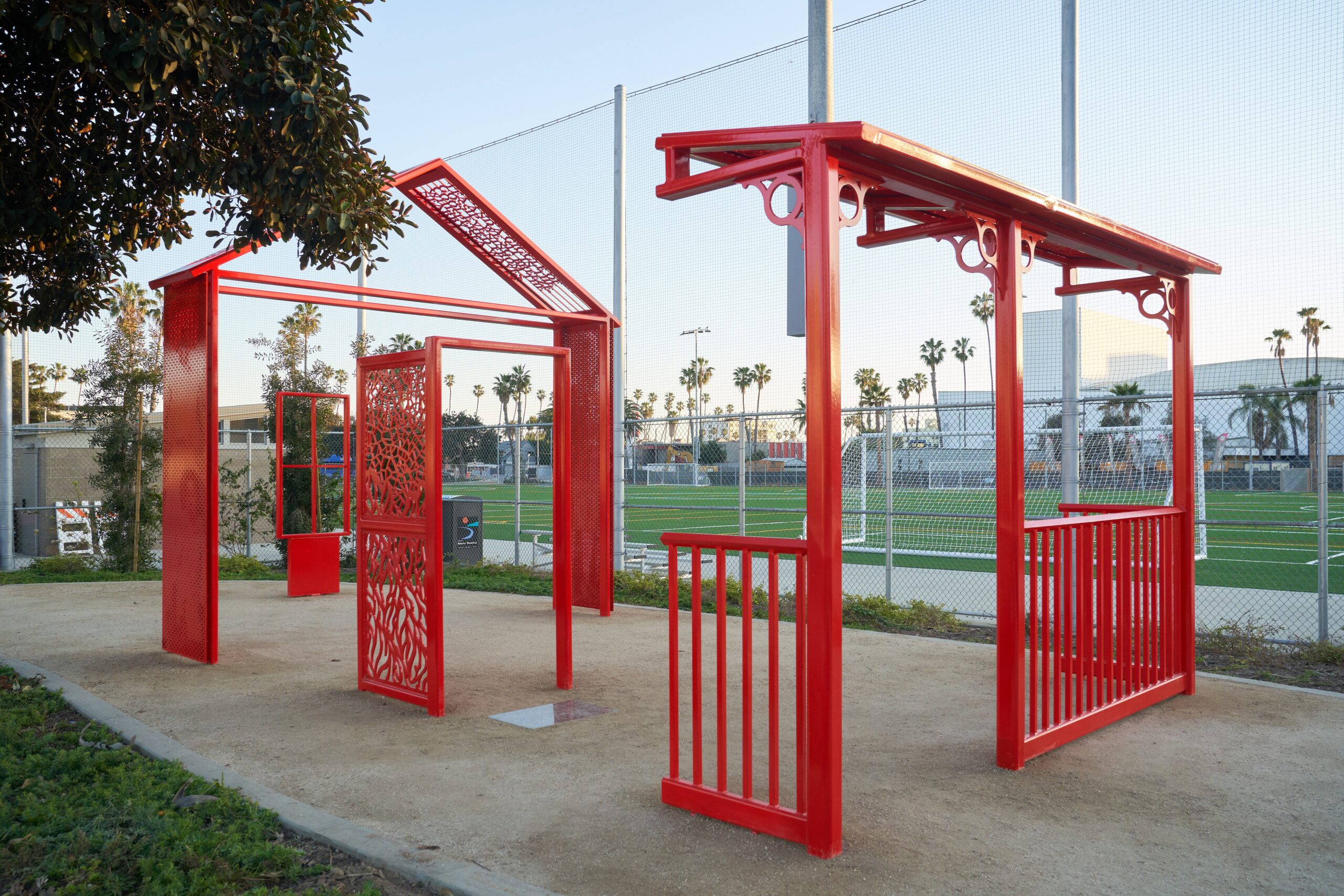 Several large red sculptures placed outside in front of a soccer field.