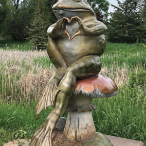 A statue of a frog perched atop a mushroom in a garden setting.