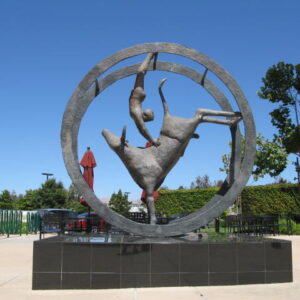 A sculpture of a human figure and a bull within a metal circle on a black base, set outdoors.