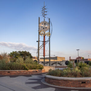 Tall sculpture with large gears surrounded by landscaped garden