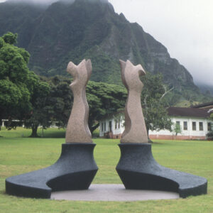 Abstract sculptures on a green lawn with misty mountains and a building in the background.