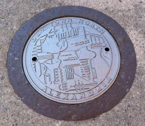 Metal manhole cover with abstract design and "Old Town North Alexandria" text.