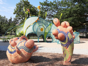 Colorful mosaic sculptures and a netted playground structure with trees in the background.