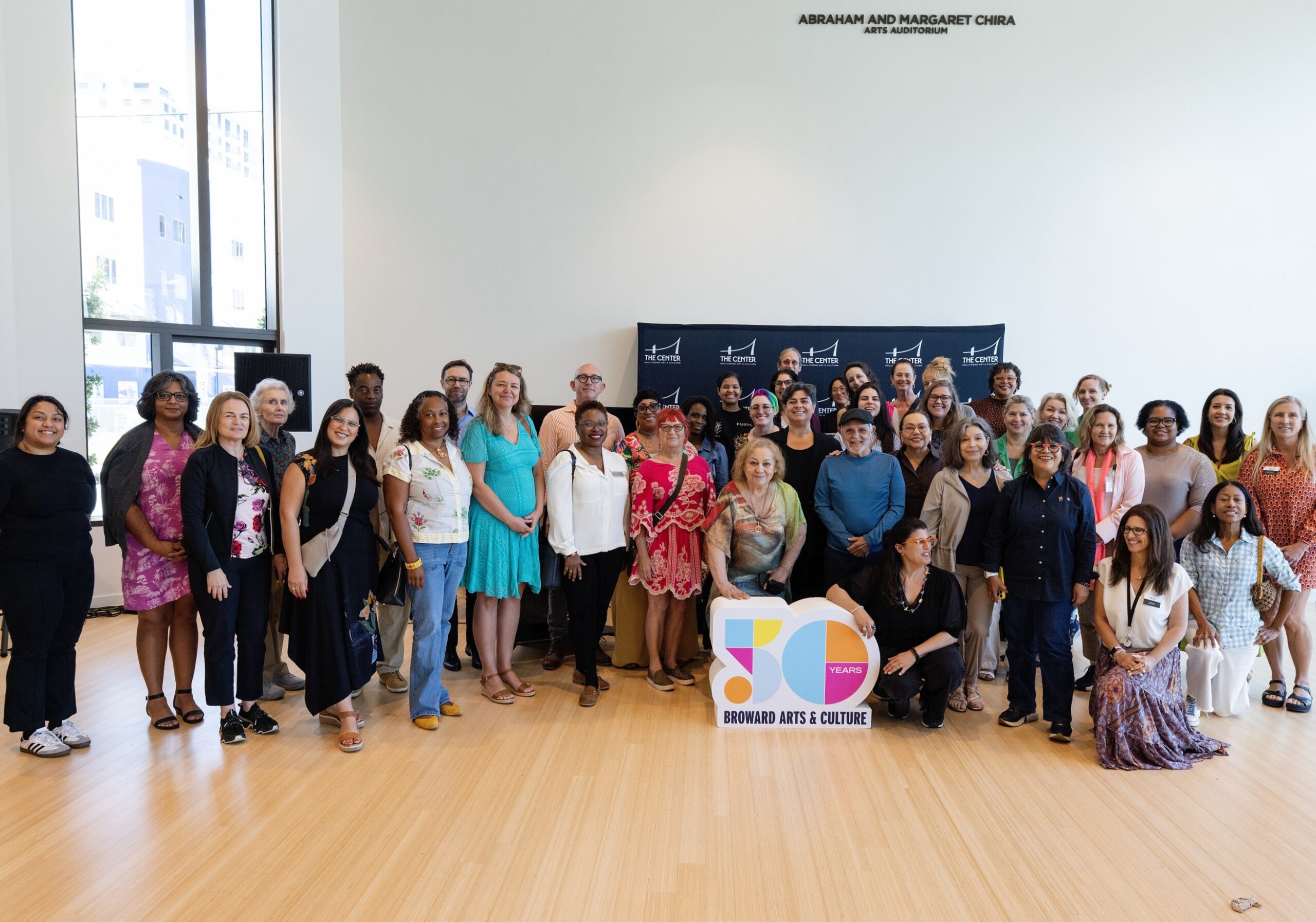 Group photo of about 30 people inside of an art gallery holding a 50th anniversary sign.
