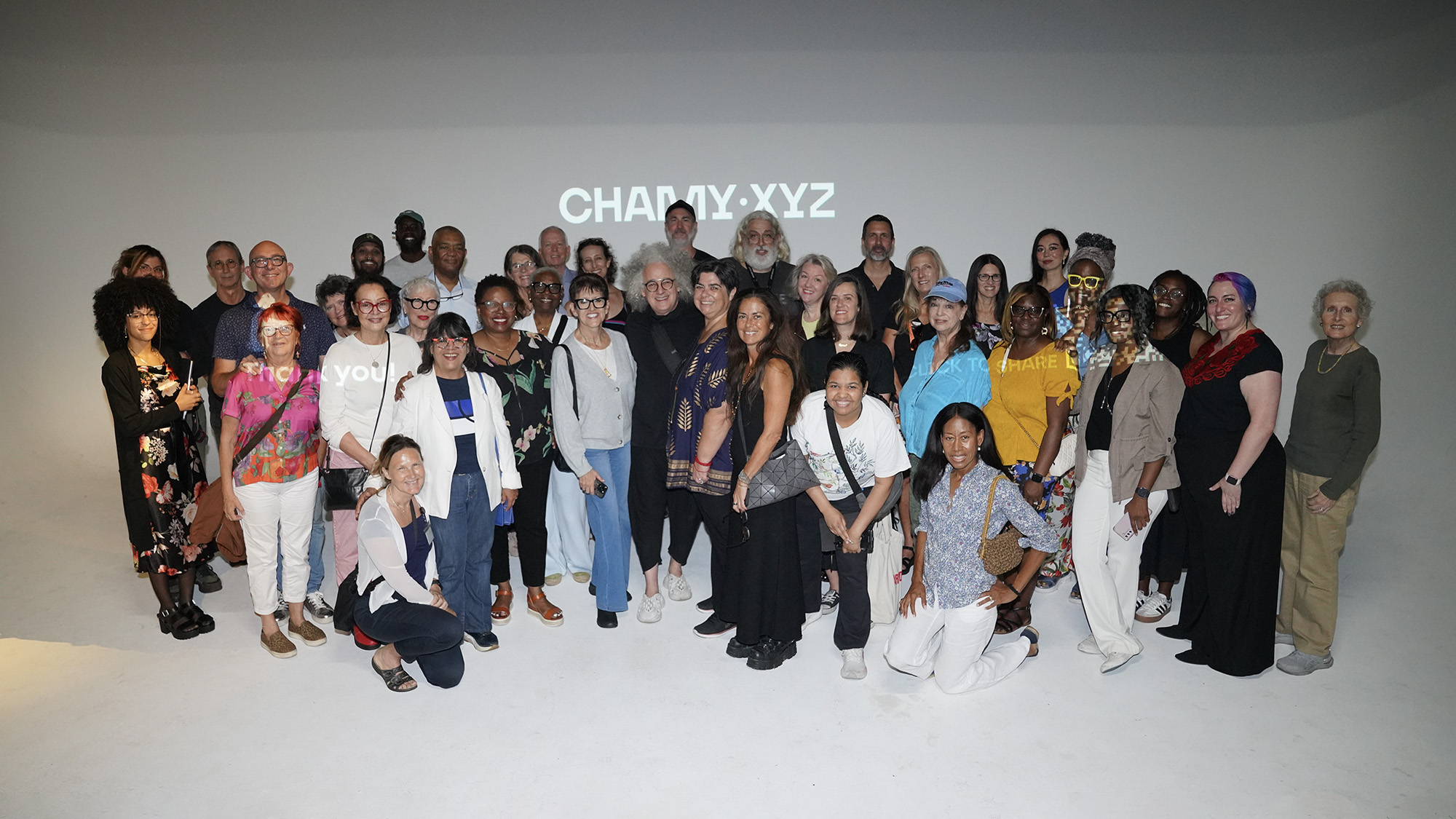 Photo of group of about 40 people standing in front of a white wall with some text from a projector on it.