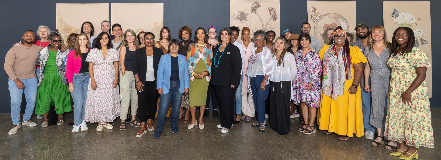 Group photo of about 30 people posed in a gallery setting with blue and gray walls